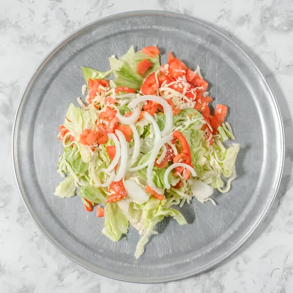 Fresh salad with lettuce, diced tomatoes, sliced onions, and shredded cheese on a metal pizza pan.