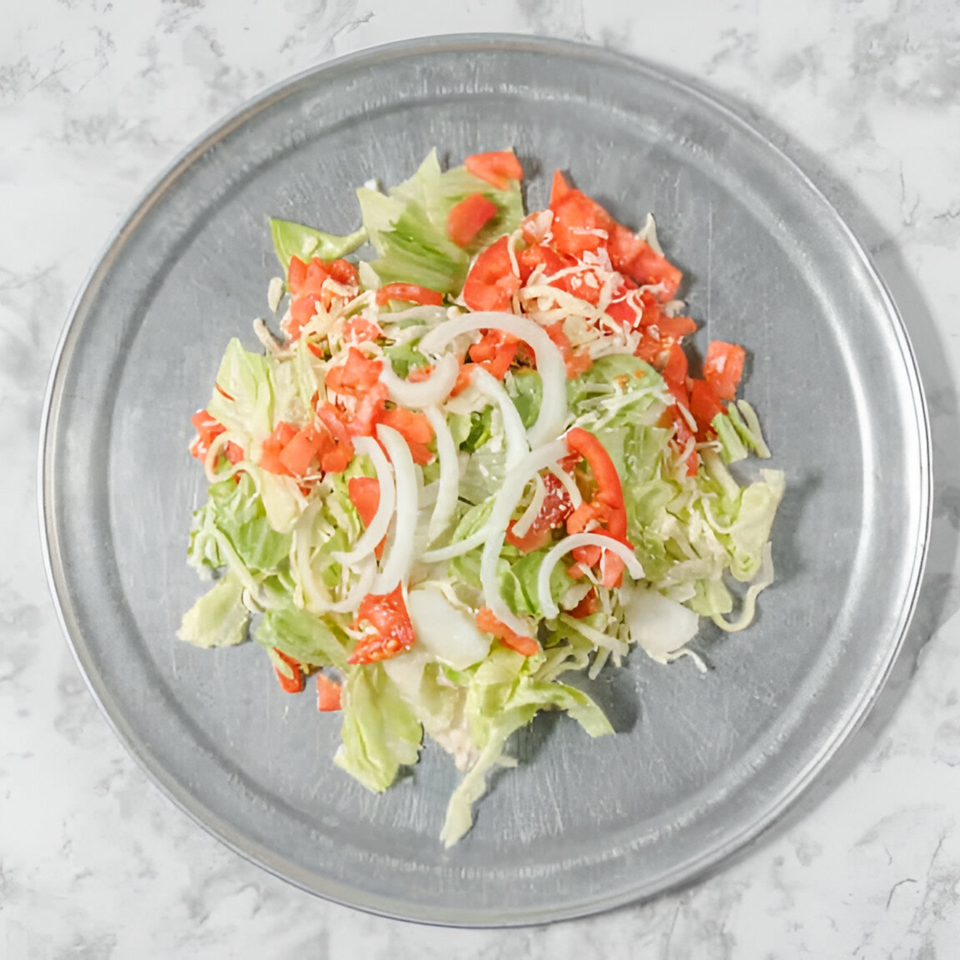 Fresh salad with lettuce, diced tomatoes, sliced onions, and shredded cheese on a metal pizza pan.