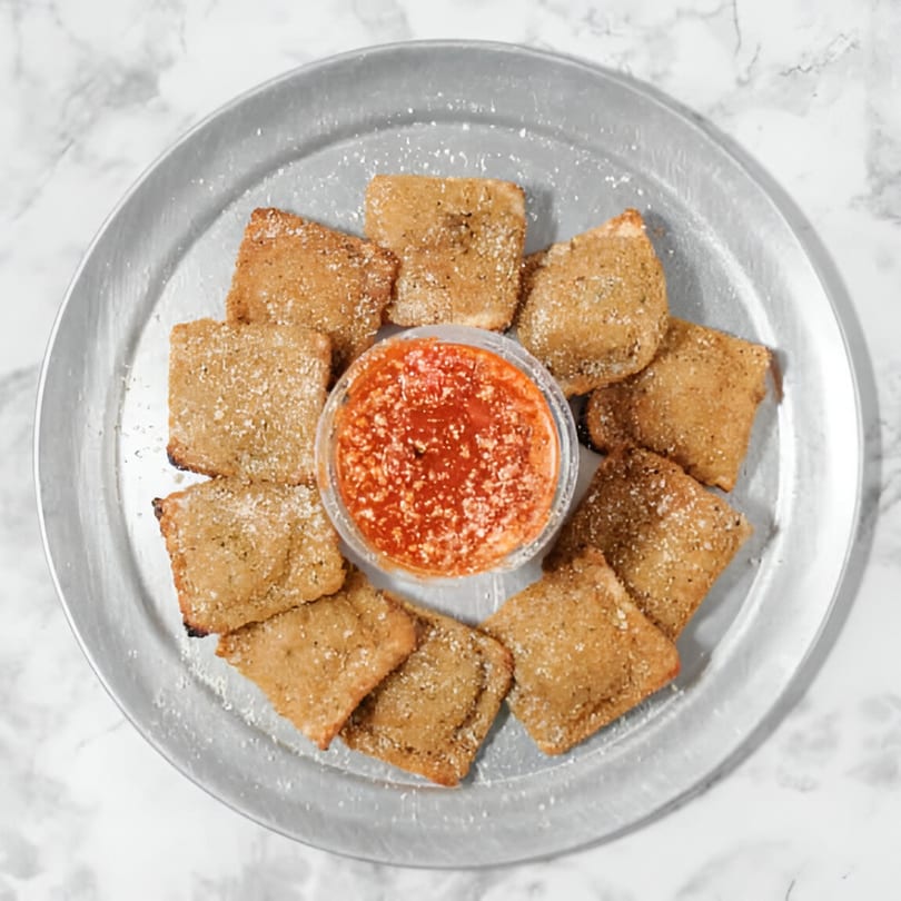 Toasted ravioli appetizer with a side of marinara sauce on a metal plate from Pointer's Pizza.