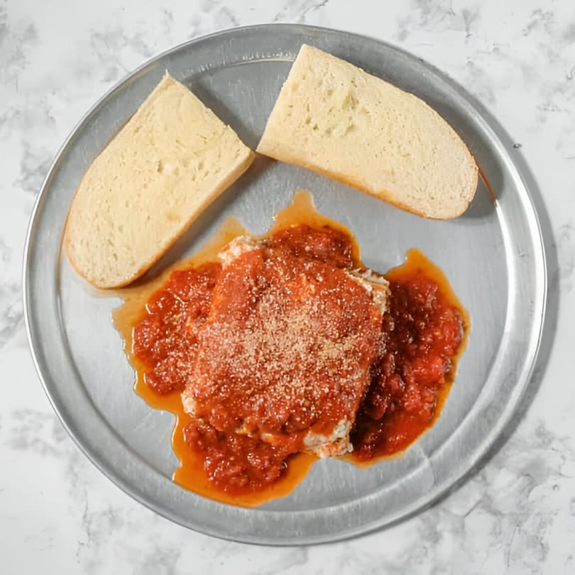 Baked lasagna with red sauce and Parmesan cheese, served with two slices of bread on a metal tray.