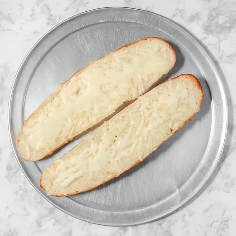 Two slices of cheesy garlic bread on a round metal pizza pan.