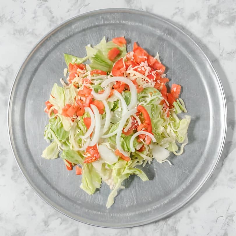 A fresh side salad with lettuce, diced tomatoes, onions, and shredded cheese on a metal plate.