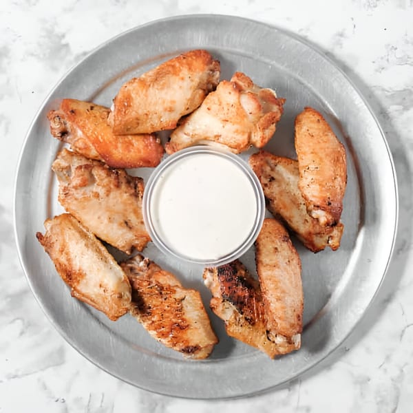 Golden brown chicken wings arranged around a small cup of white dipping sauce on a metal tray.