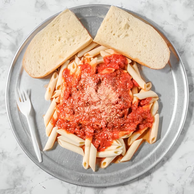 Penne pasta with red sauce and Parmesan cheese, served with two slices of bread on a metal tray.